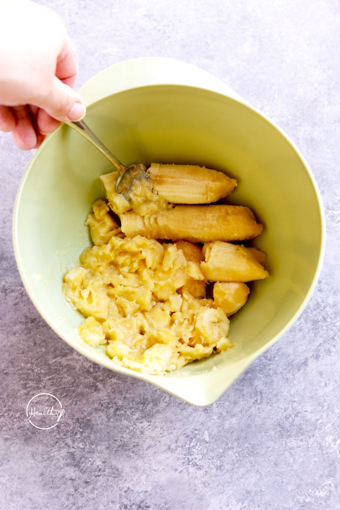 mashing bananas with a fork in a green bowl