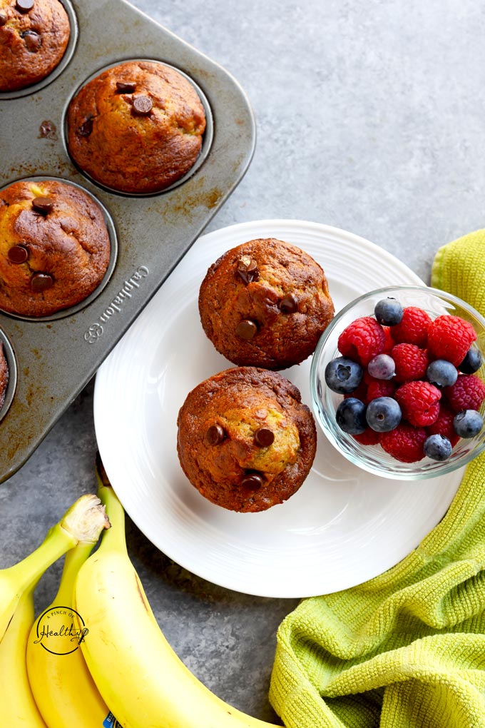 Banana chocolate chip muffins on a white plate with berries on a gray background