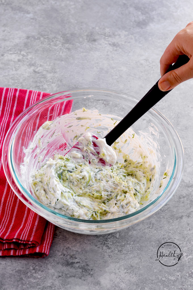 Mixing up homemade Tzatziki sauce in a clear bowl with a red towel