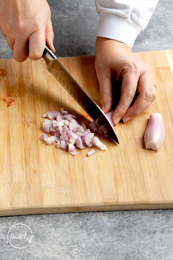 hands slicing shallot on wood cutting board