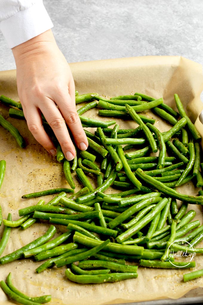 hand tossing green beans in olive oil and seasonings