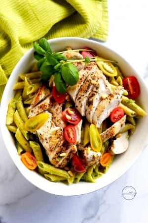 chicken pesto pasta in a white bowl on a marble surface with green towel