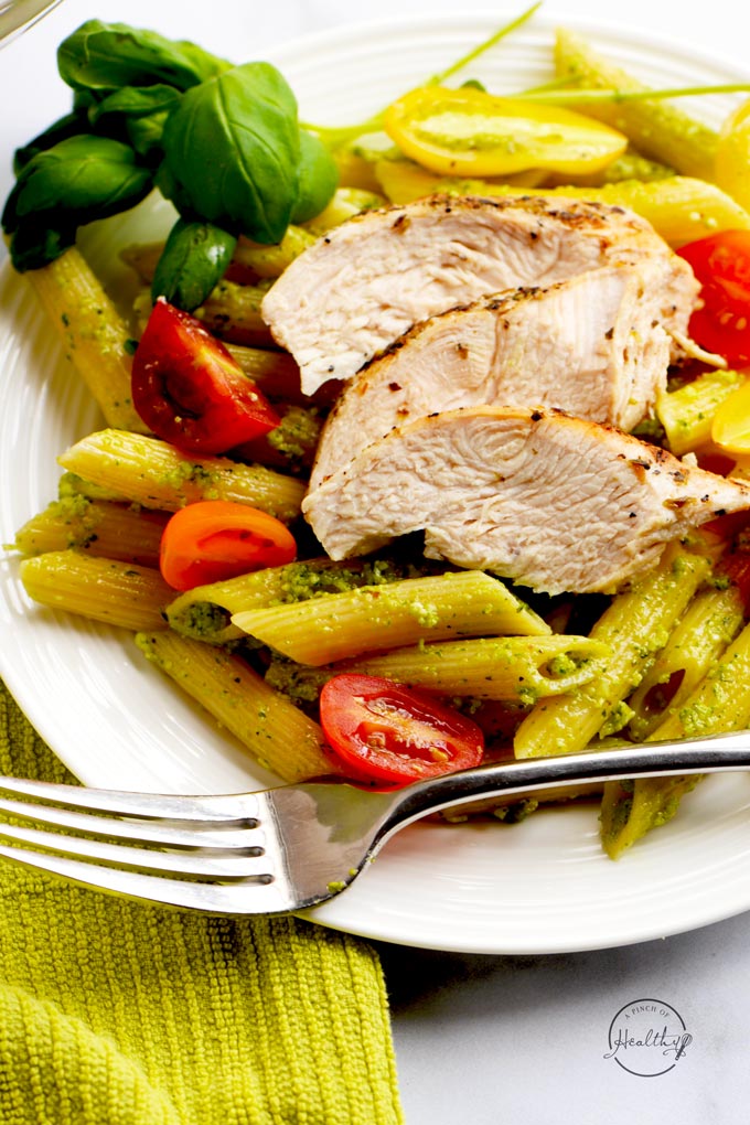 closeup chicken pesto pasta on white plate with fork