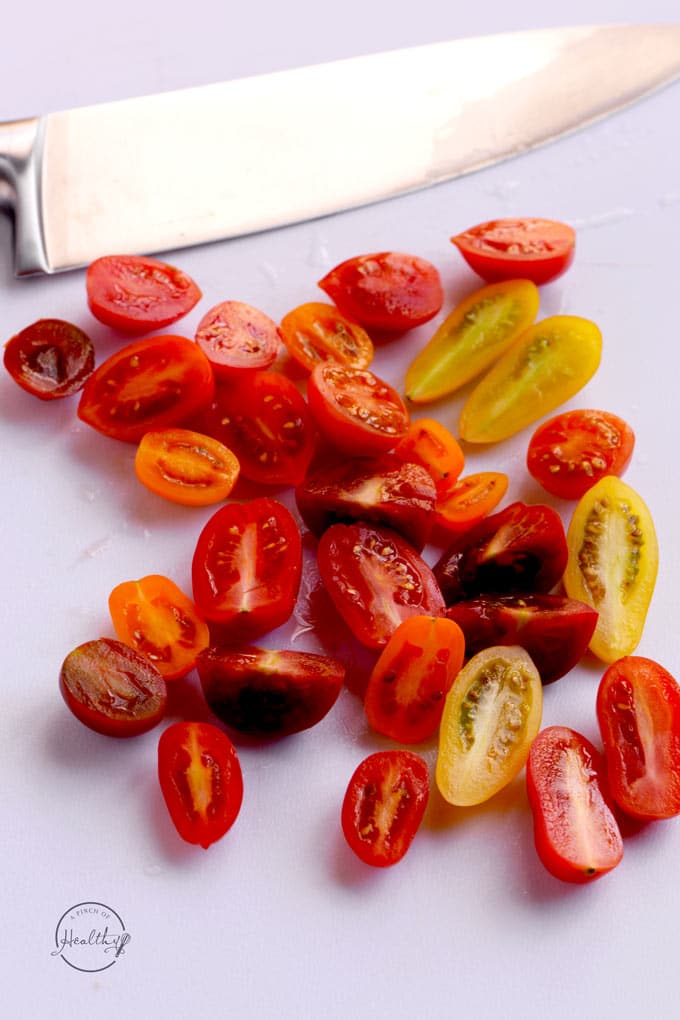baby heirloom rainbow tomatoes halved on a white cutting board