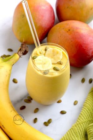 mango smoothie with bananas and pumpkin seeds on a white surface with green towel