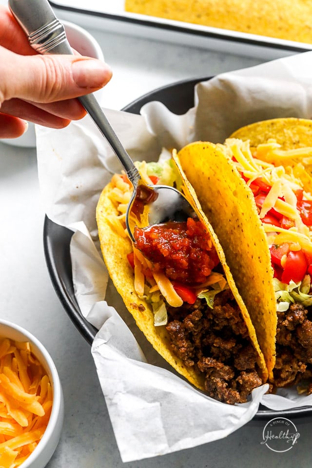 hand spooning salsa onto ground beef tacos
