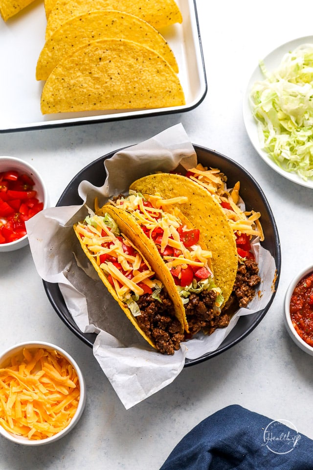 ground beef tacos on white surface with additional toppings in small bowls