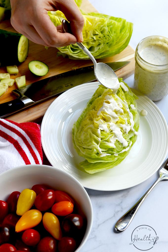 Hand spooning ranch dressing onto iceberg lettuce wedge