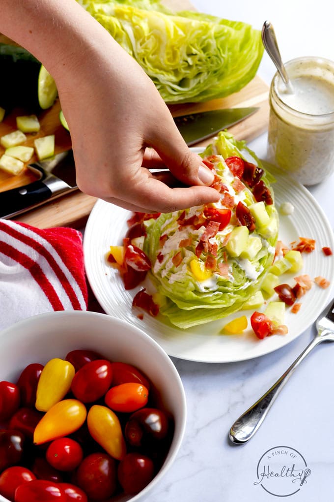 hand sprinkling bacon on wedge salad