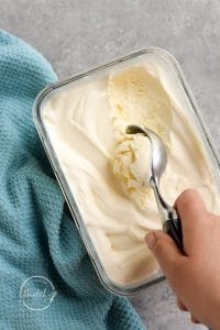 Hand scooping vanilla ice cream on gray counter with blue towel