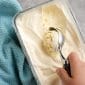 Hand scooping vanilla ice cream on gray counter with blue towel