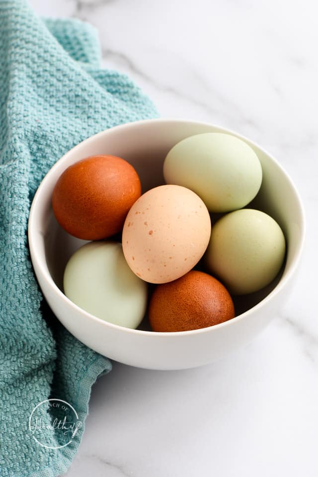 multi colored eggs in a white bowl with blue towel