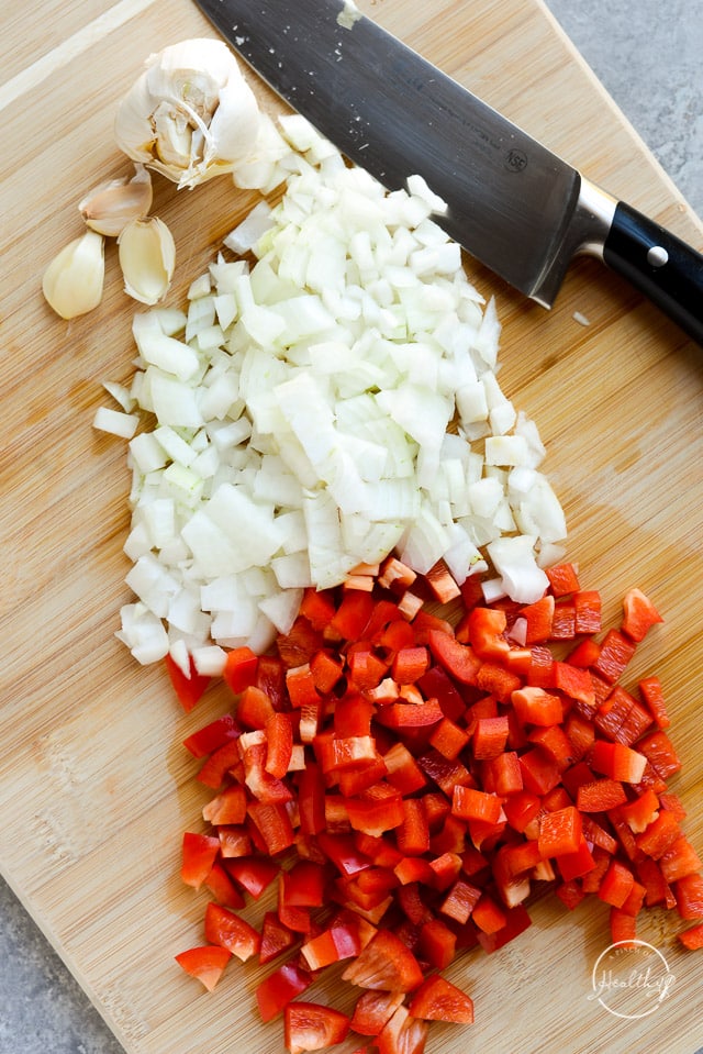 diced red bell pepper and onion on a wooden cutting board with a knife