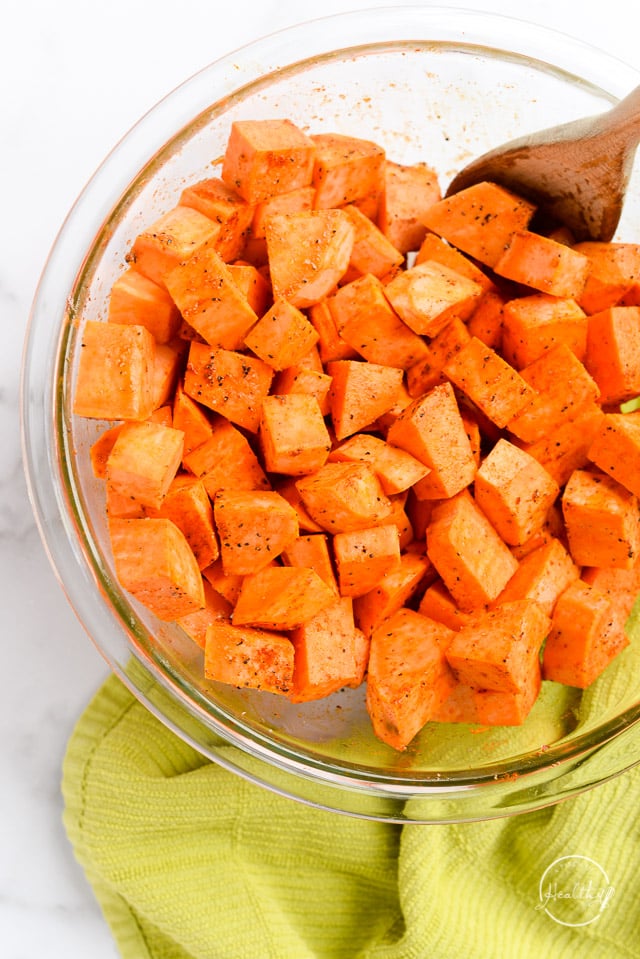 clear glass bowl with sweet potatoes tossed in oil and seasonings