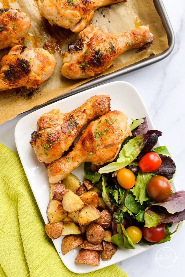 Baked chicken drumsticks overhead on marble table with salad and potatoes