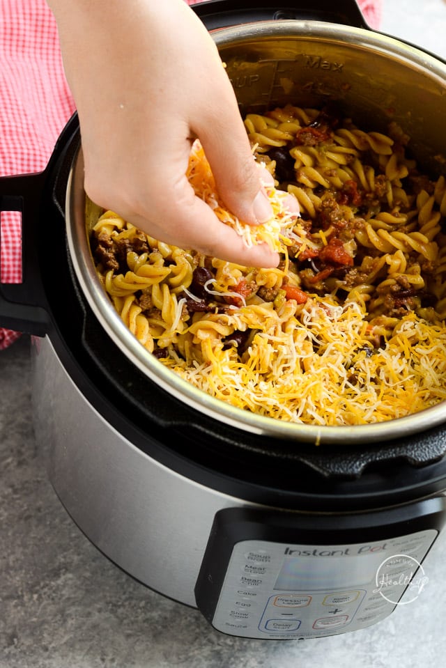 Hand sprinkling cheese on top of Instant Pot chili mac