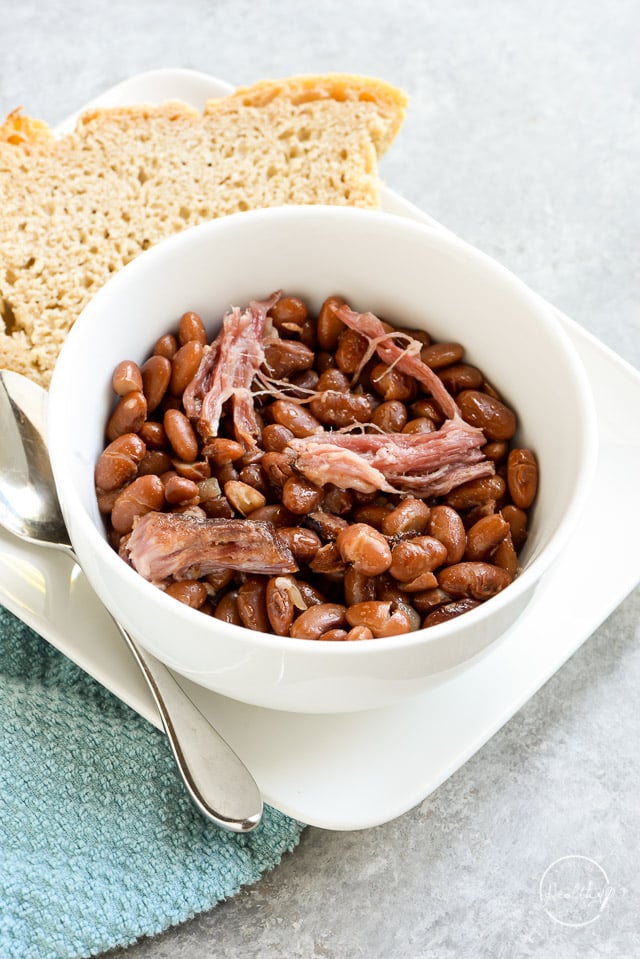 Crock pot pinto beans with ham in a white bowl with a side of sourdough bread