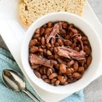 Crock pot pinto beans with ham in a white bowl with side of sourdoughbread