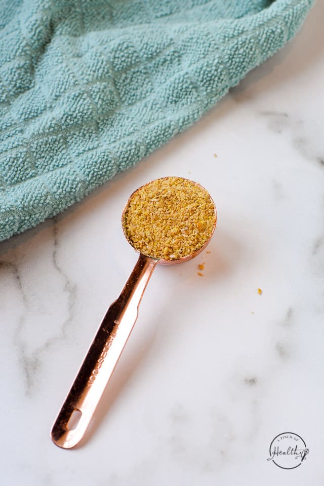 ground flax seed in a copper Tablespoon on a marble surface with turquoise towel