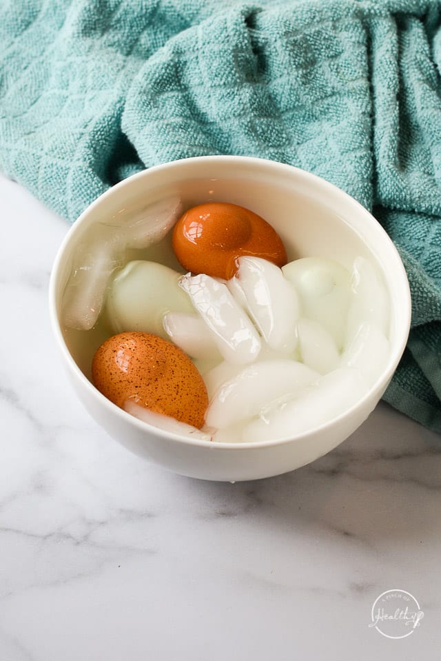 Cooked eggs cooling in a white bowl of ice water on marble counter