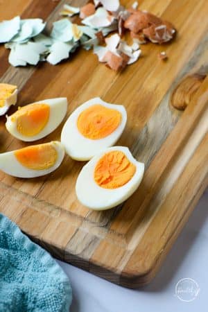 air fryer hard boiled eggs sliced on a cutting board with shells in the background with a blue towel