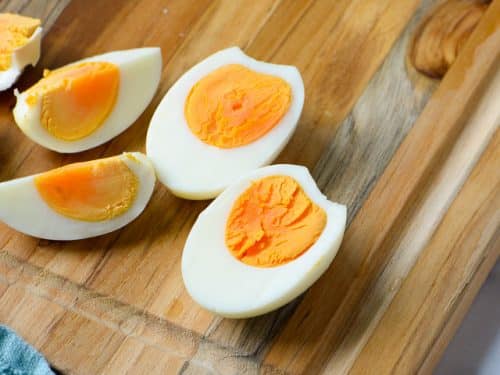 air fryer hard boiled eggs sliced on a cutting board with shells in the background with a blue towel