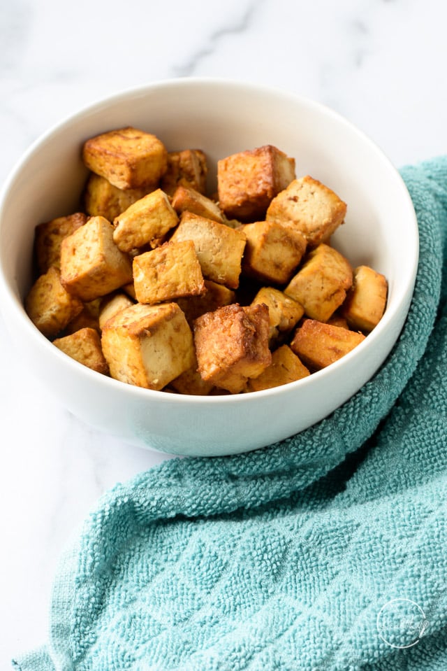Air Fryer tofu in a while bowl with a blue kitchen towel
