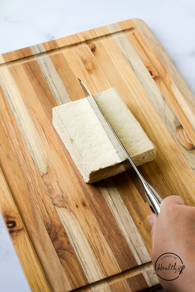 knife cutting tofu in half on wood board