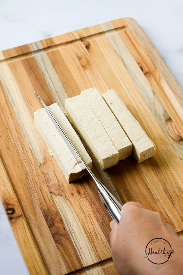 hand with knife cutting tofu on wood board
