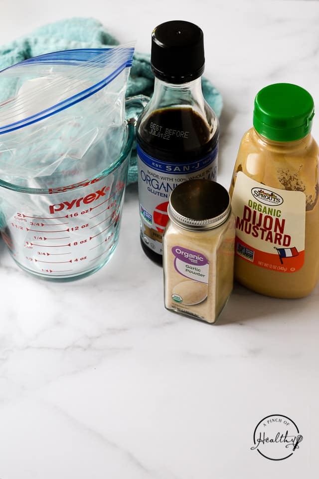 garlic powder, Tamari and dijon mjustard next to glass pyrex measuring cup lined with freezer bag