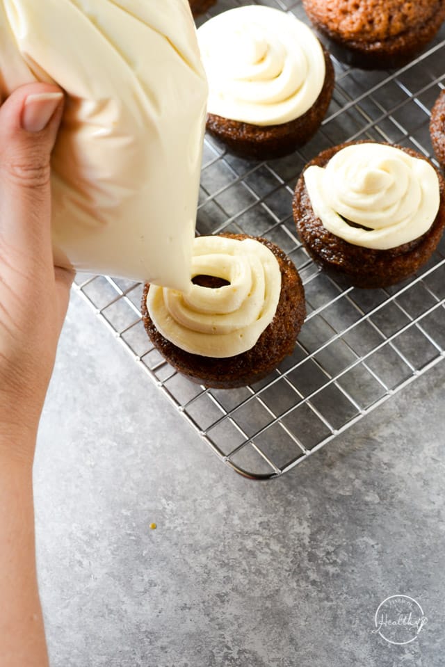 hand piping cream cheese icing onto carrot cake cupcakes