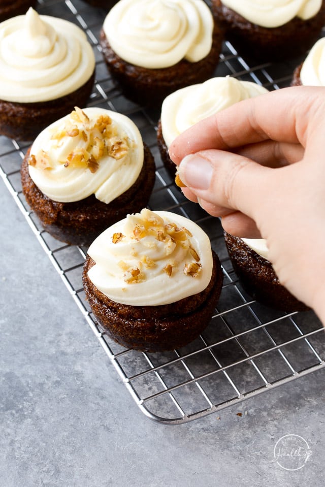 hand sprinkling chopped walnuts on carrot cake cupcakes