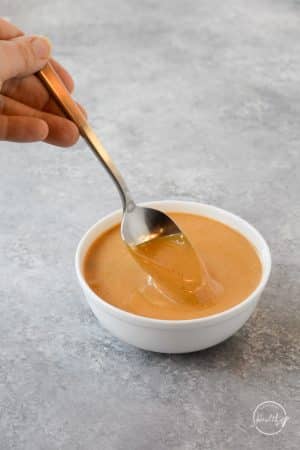 Hand spooning Thai peanut sauce in white bowl