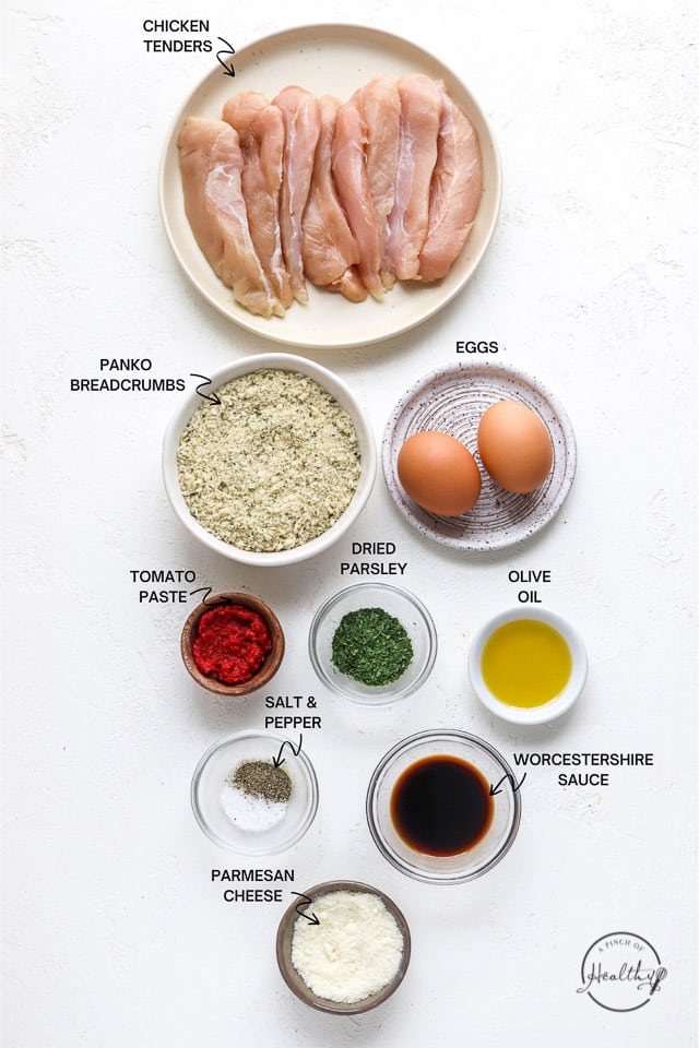 Raw chicken, bread crumbs, eggs and spices on a white countertop