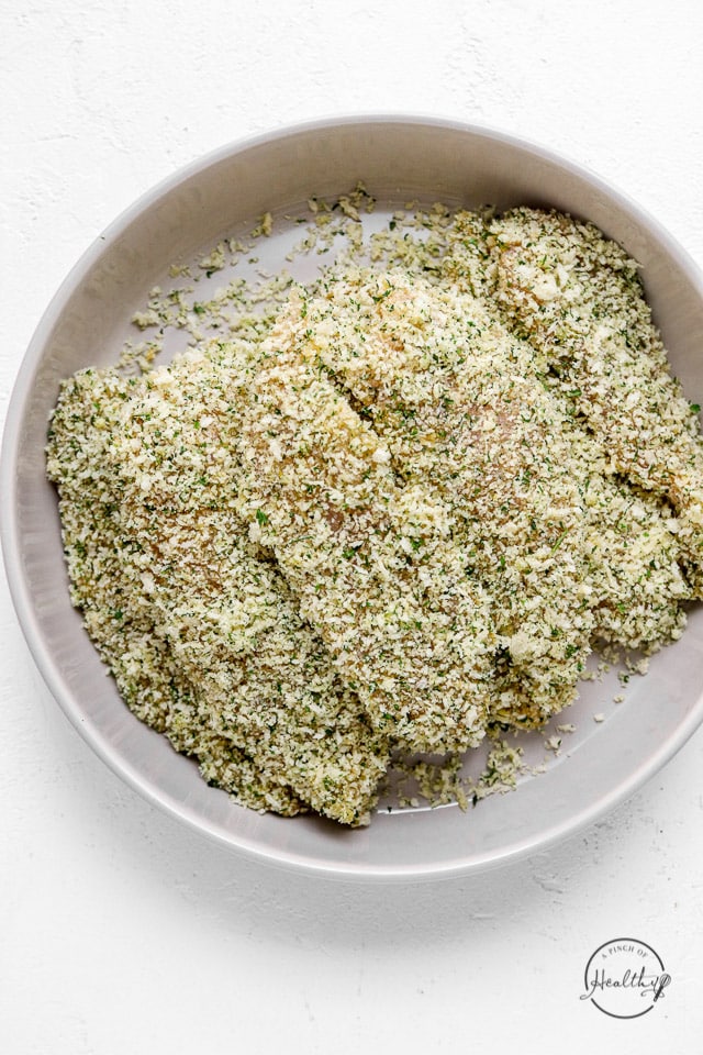 dredged and breaded raw chicken tenders on white plate