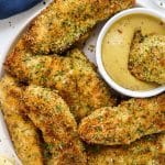 Plate of crispy chicken tenders with one being dipped in honey mustard sauce