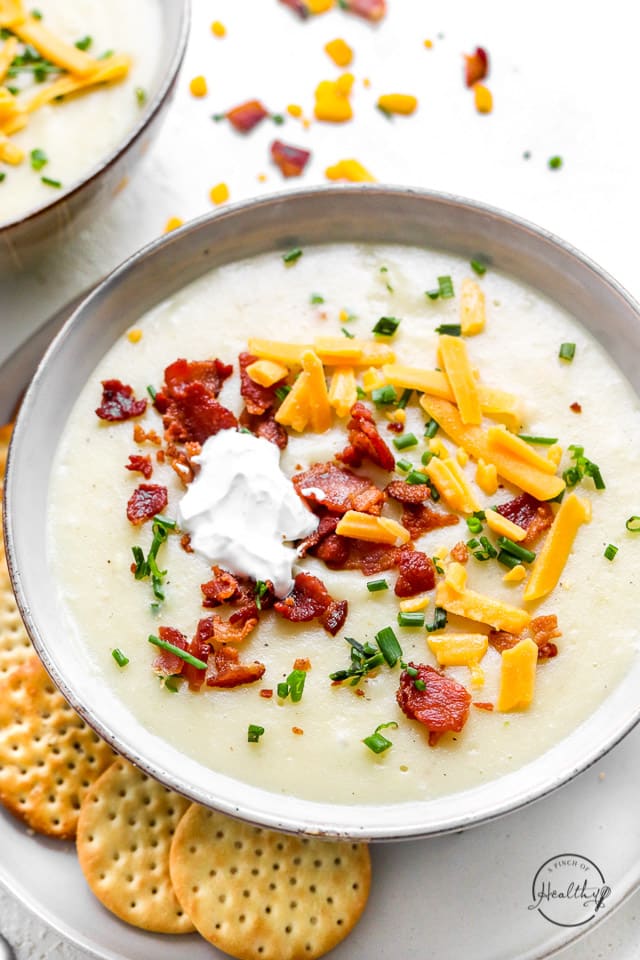 Creamy potato soup, with toppings in a white bowl with crackers