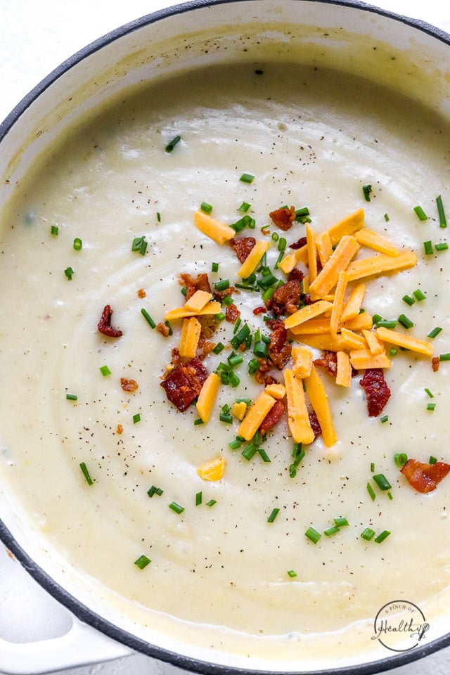 creamy potato soup in big pot topped with bacon, cheese and sour cream