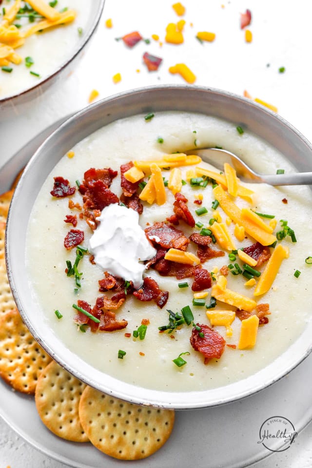 creamy potato soup with bacon bits, cheese, chives and sour cream with spoon in a bowl