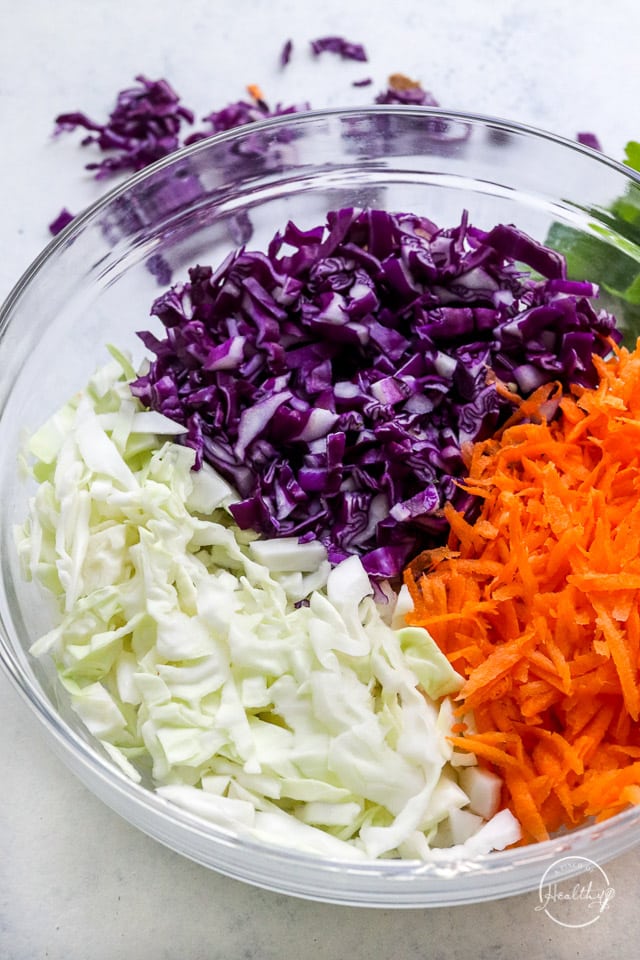shredded purple cabbage, green cabbage and carrots in a clear glass bowl