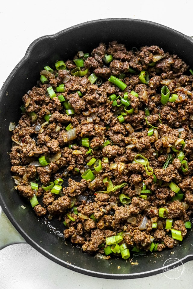 seasoned and cooked ground meat in a skillet topped with green onion