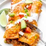 fork cutting into beef enchiladas on a white plate with slice of lime on the side