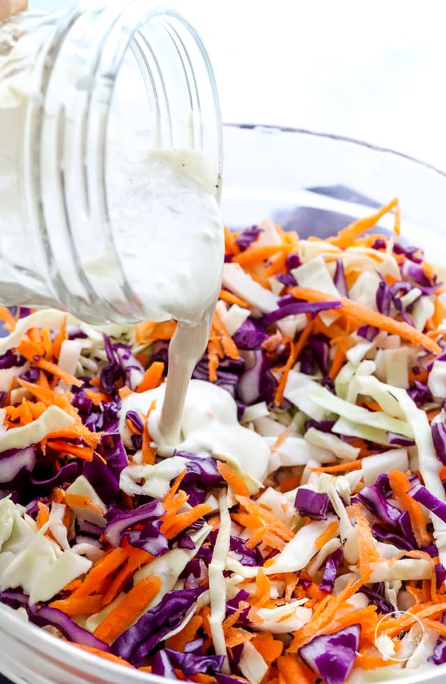 pouring homemade dressing over veggies to make creamy coleslaw