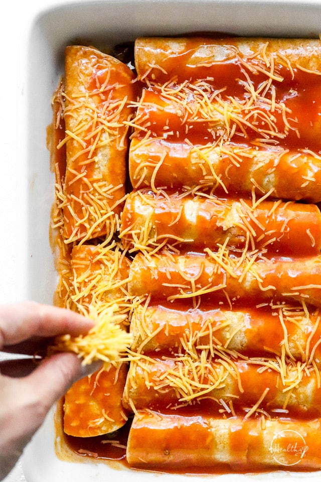 hand sprinkling cheese on casserole dish full of beef enchiladas