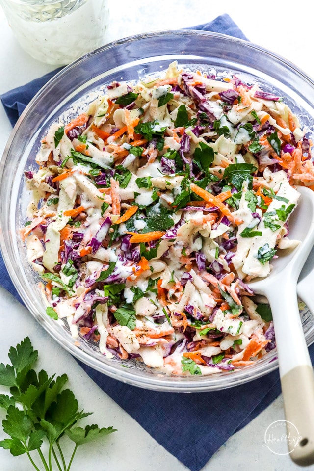 creamy coleslaw in a clear glass serving bowl with wooden spoon