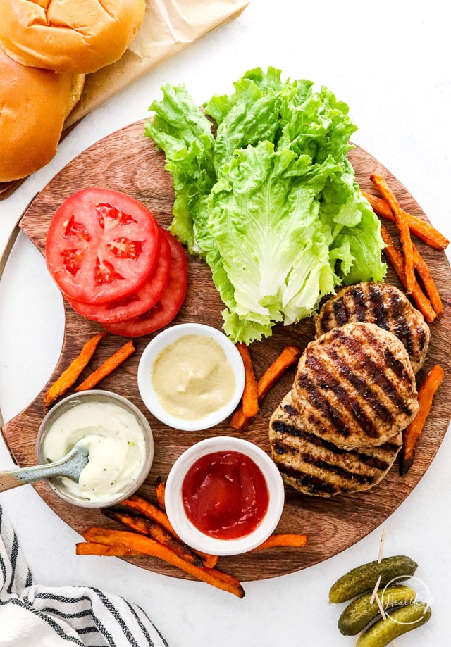 grilled turkey burger patties on wood platter with toppings - lettuce, tomato, ketchup, mustard and mayo