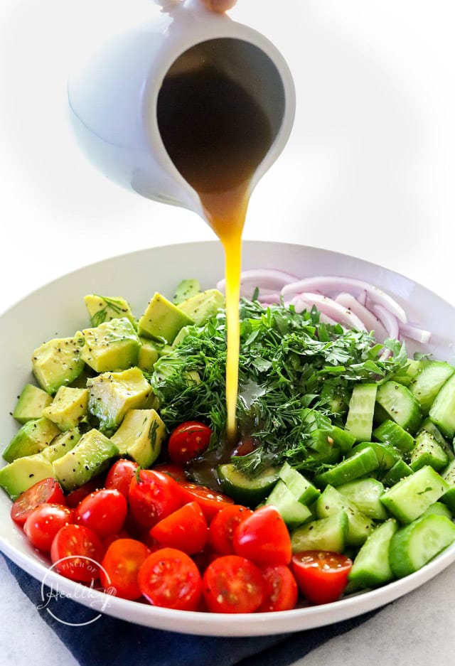 pouring dressing over tomtato cucumber and avocado salad
