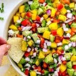 hand dipping tortilla chip into mango salsa