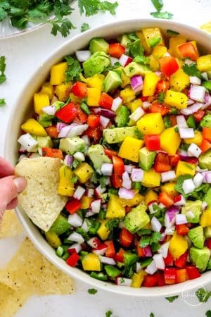 hand dipping tortilla chip into mango salsa