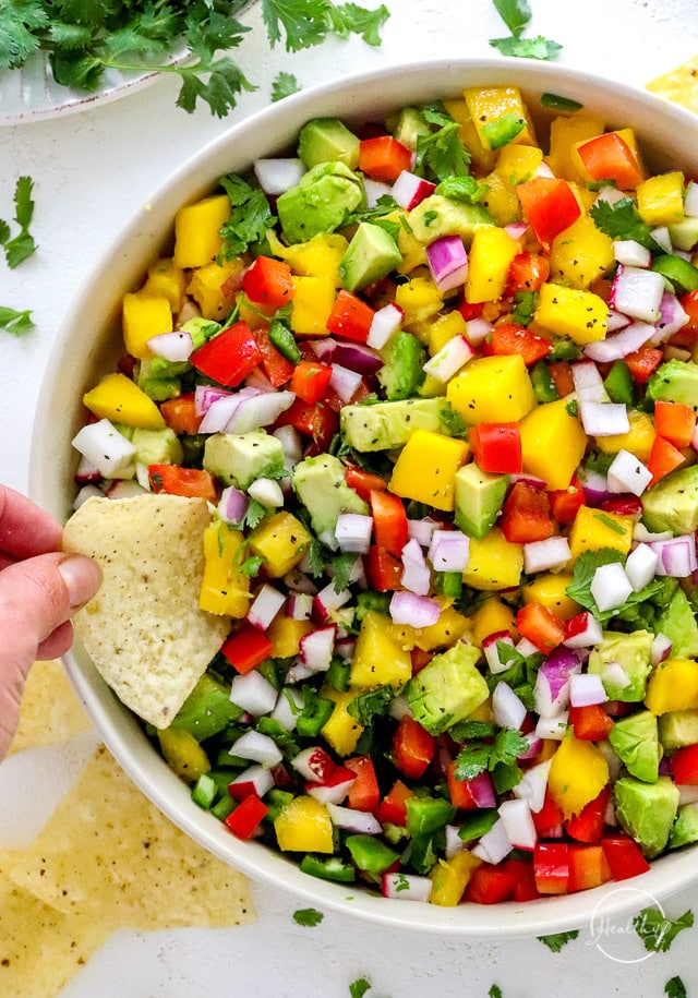 hand dipping tortilla chip into mango salsa